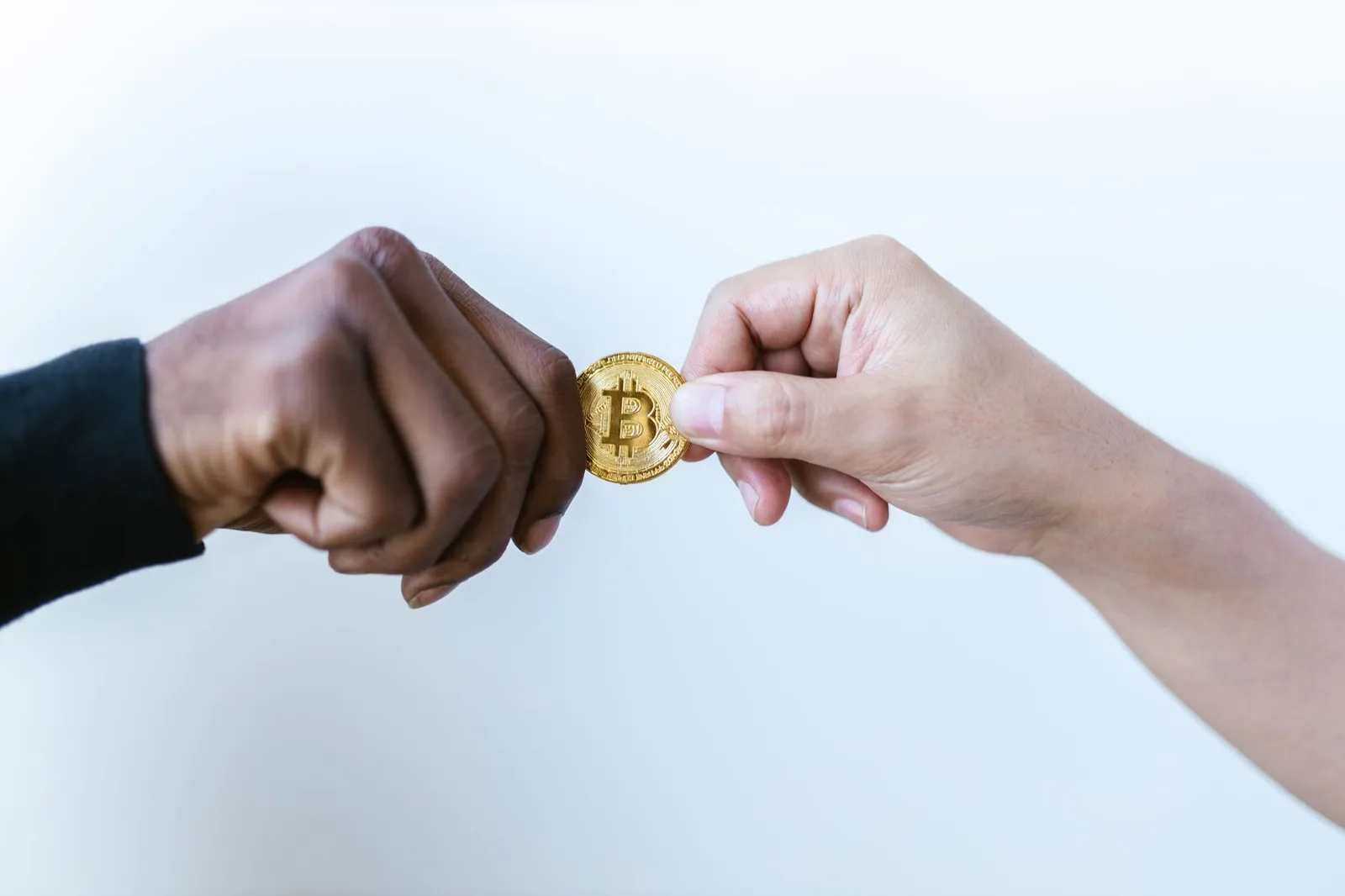 Dos manos intercambiando una moneda de Bitcoin, simbolizando transacciones de criptomonedas.